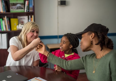 A parent, teacher, and student fistbump and smile. 