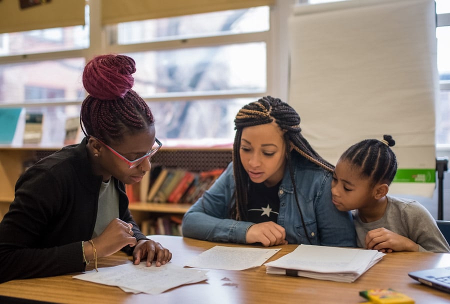 A parent, student, and teacher sit around a table looking down at paperwork