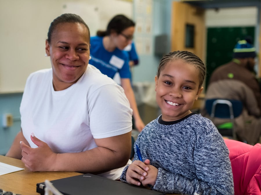 A girl and her family partner sit at a table and smile. A girl and her family partner sit at a table and smile.