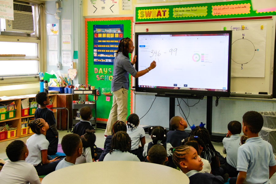 A male teacher writes on an electronic whiteboard while a class of kindergarten students watch. A male teacher writes on an electronic whiteboard while a class of kindergarten students watch.